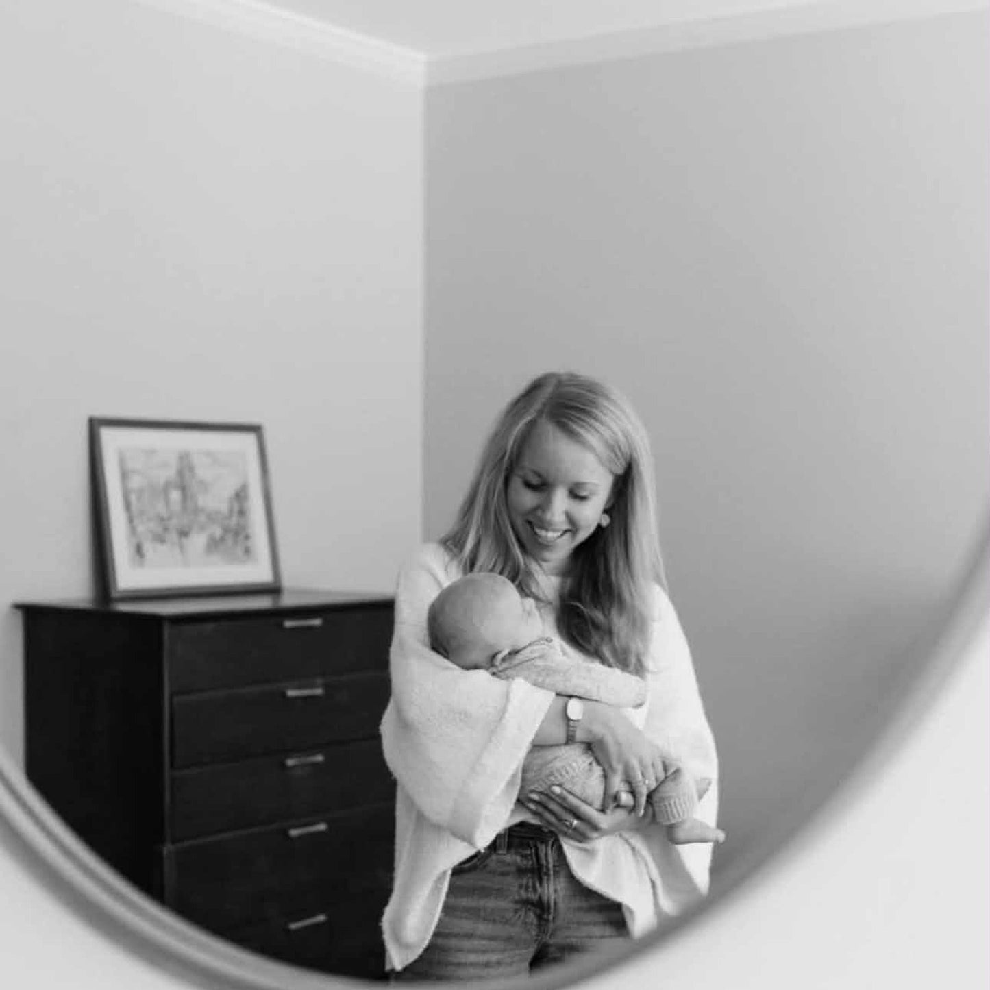 Katie Halabrin holding her newborn son, reflected in a round mirror