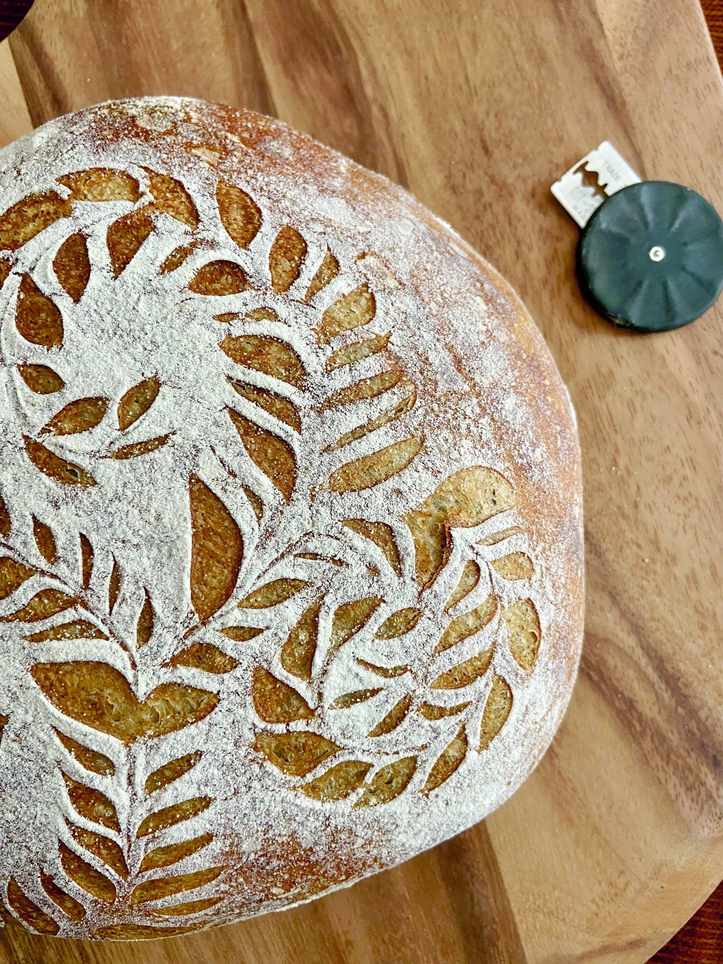 Sourdough loaf scored with a fern and leaf design, beside a Wire Monkey Corbeau lame. Photo by Renee Pullen.