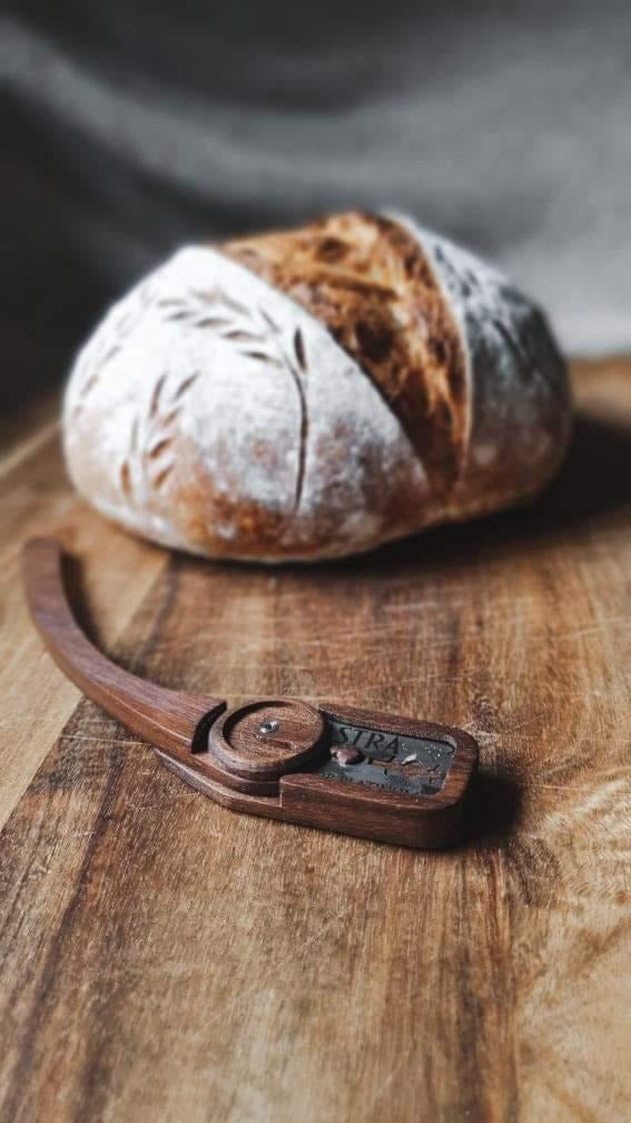 Flour-dusted sourdough boule showing a single expansion slash and wheat-stalk detail, beside a Wire Monkey Goose lame